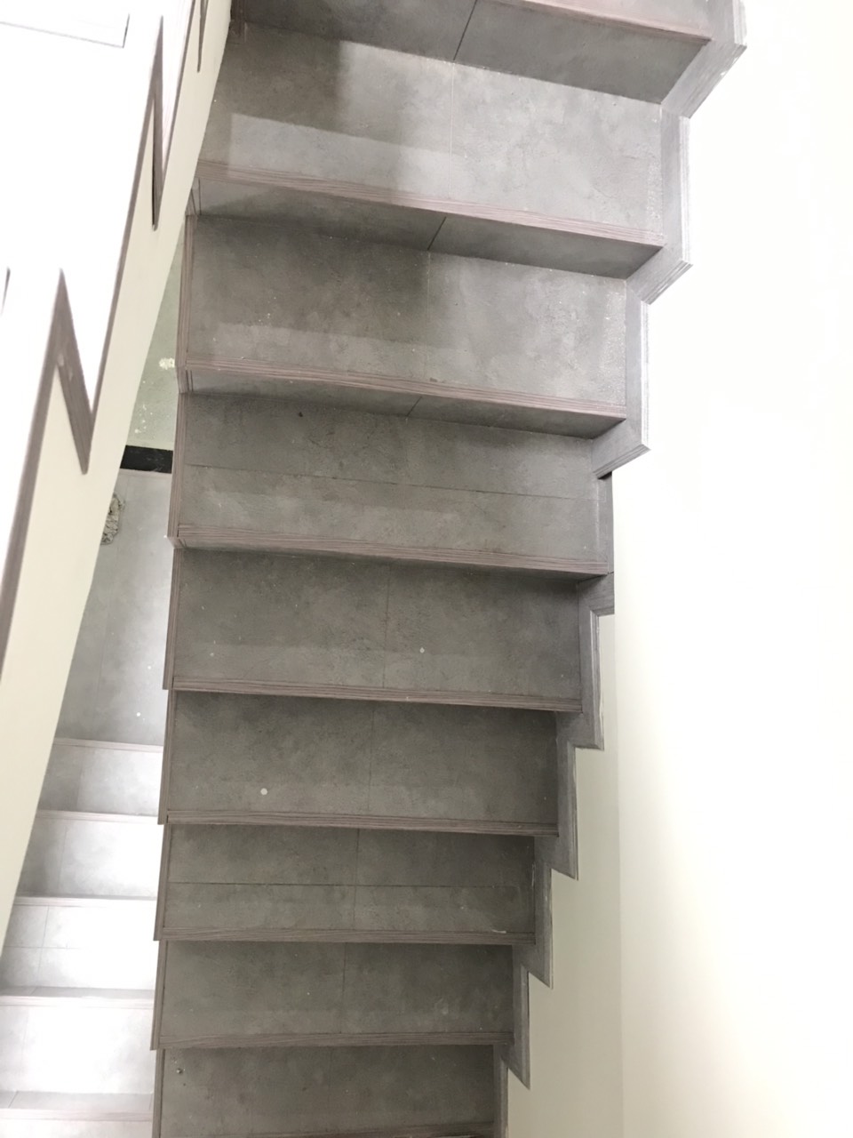 Gầu cầu thang nhà phố tại TP.HCM sau khi dán giấy dán tường tone sáng, bổ trí kệ sách gỗ và đèn LED âm bậc